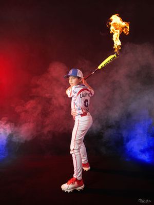 Little league player with flaming bat poses against red and blue smoke effects.