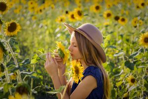 A person in a hat smells sunflowers in a golden field on a sunny day.