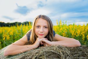 A person rests on a hay bale with yellow flowers in the background.