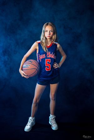 Basketball player in blue jersey number 5 posing with ball against dark backdrop with dramatic lighting.