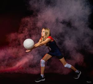 Volleyball player in blue uniform making diving save in dramatic smoke-filled studio setting.