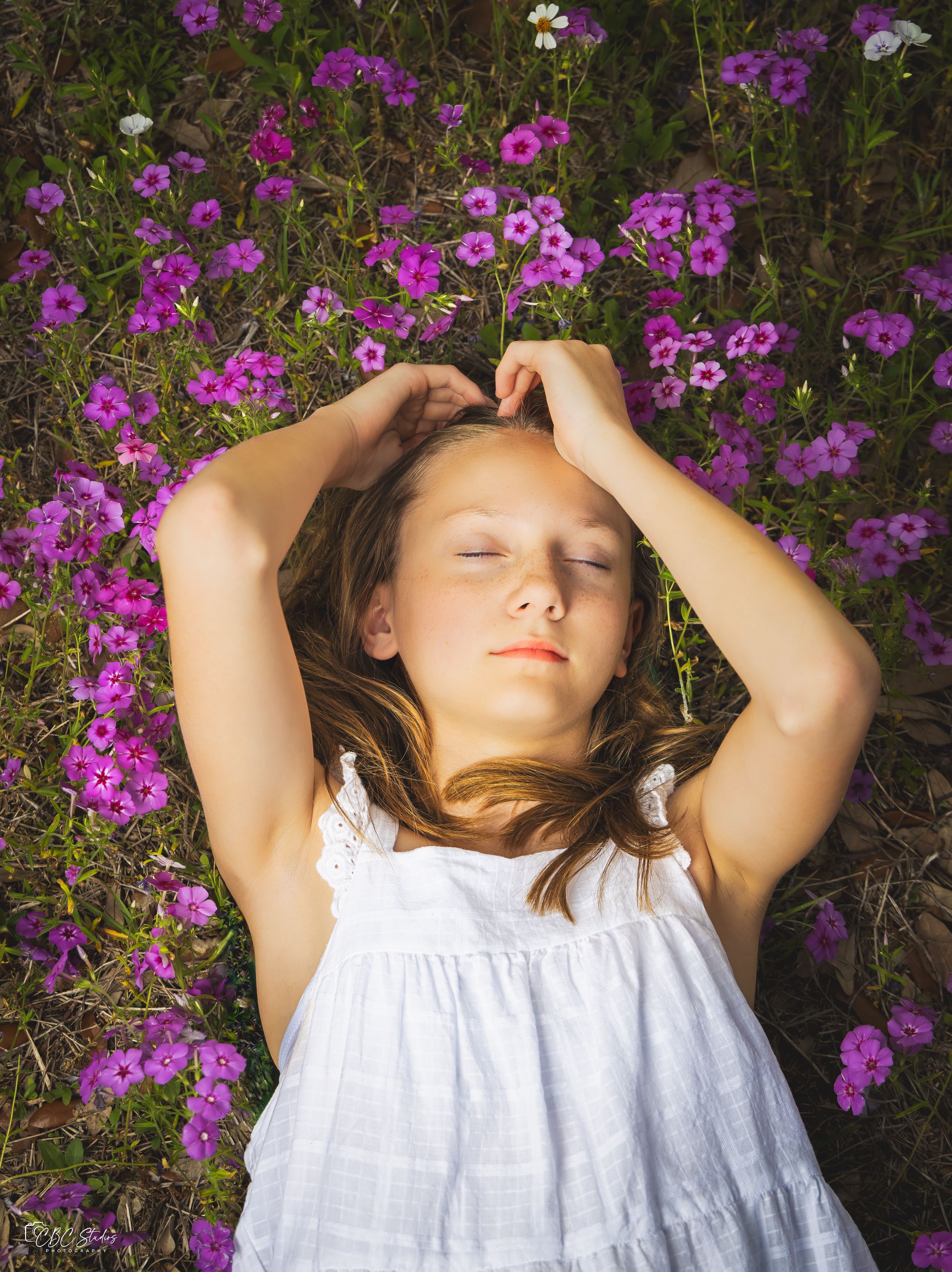 Young person in white dress lying among purple wildflowers in peaceful pose.