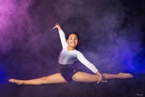 Gymnast performs a dramatic splits pose in purple and blue atmospheric smoke.