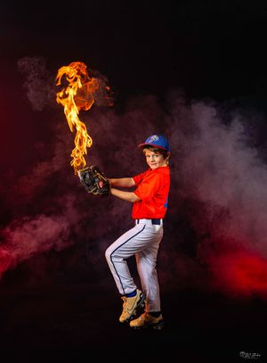 Baseball player poses with dramatic fire effect against red and black backdrop.