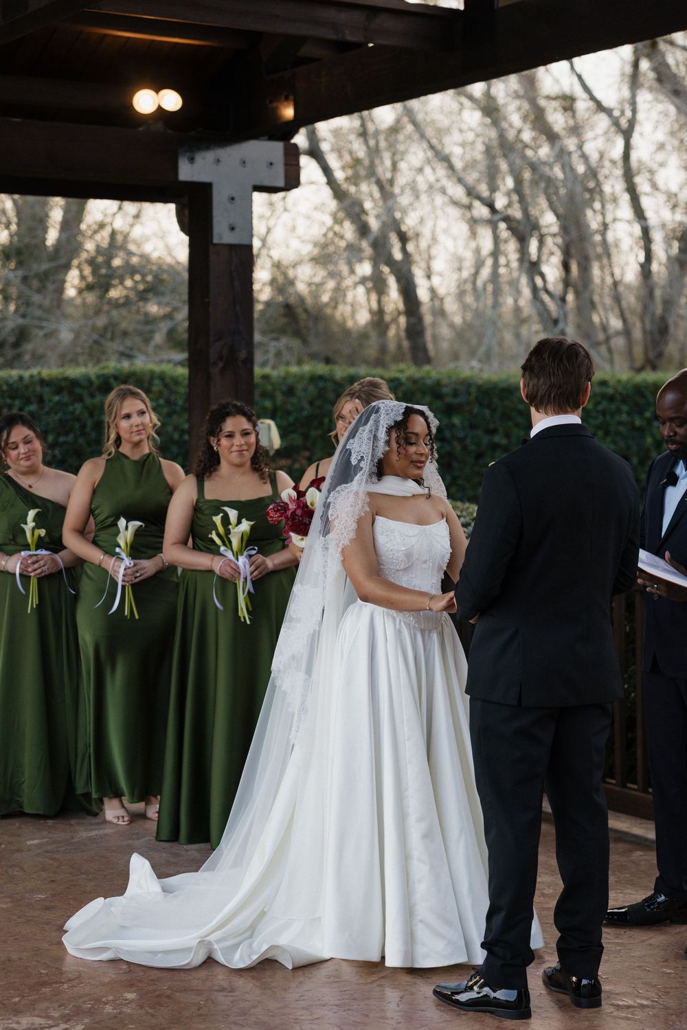 Wedding party stands in formation with bridesmaids in elegant olive green dresses and a flowing white bridal gown.