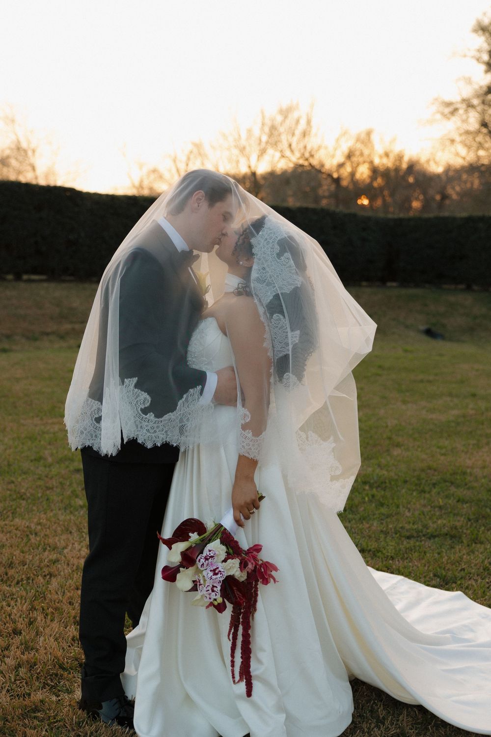 Romantic wedding couple embracing in a field at sunset with flowing white dress and veil.