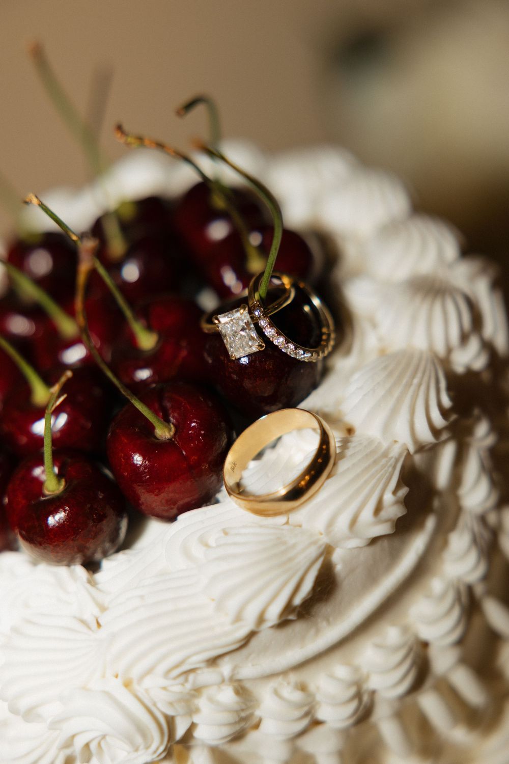 Wedding rings rest atop white frosting and fresh cherries on an elegant wedding cake.