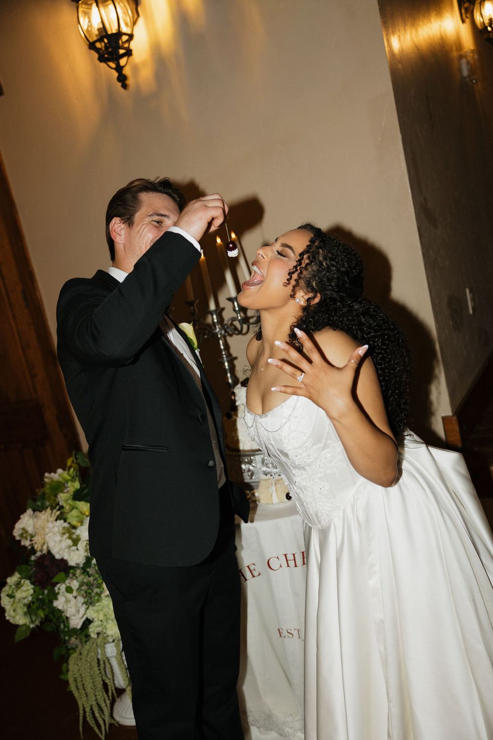 A wedding couple shares an intimate kiss under warm lighting while wearing traditional white gown and black suit.