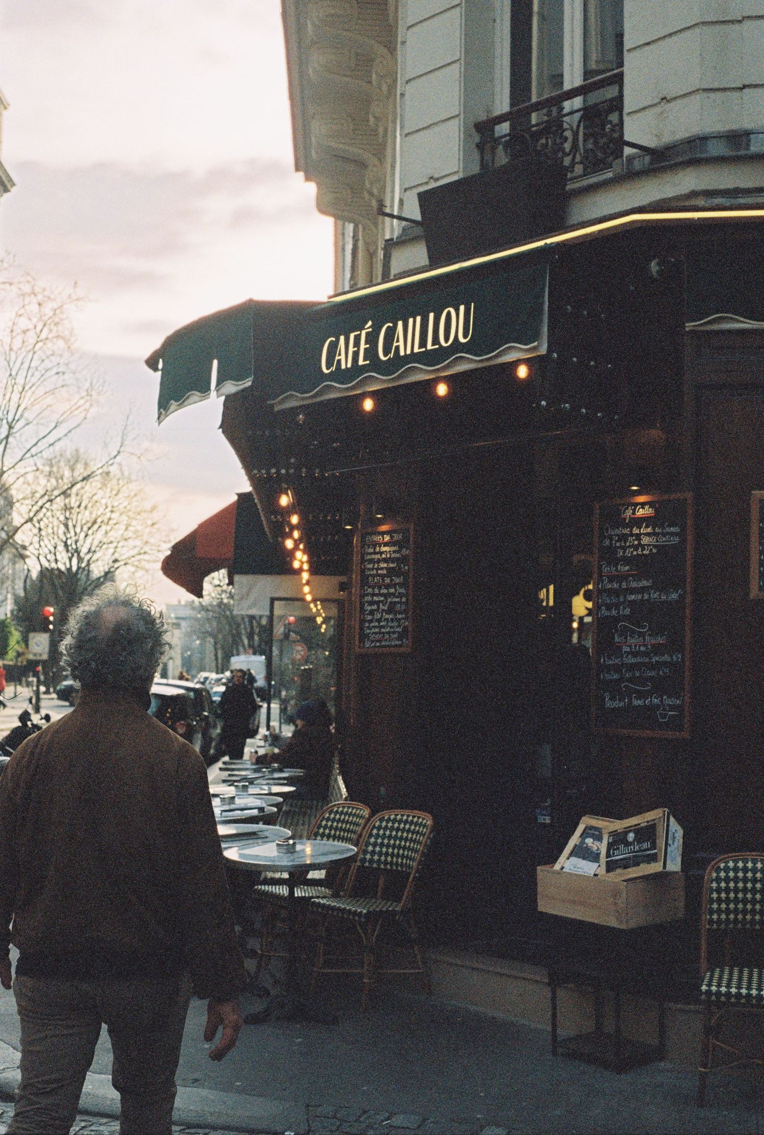 Cozy Parisian cafe with outdoor seating and illuminated signage at dusk.