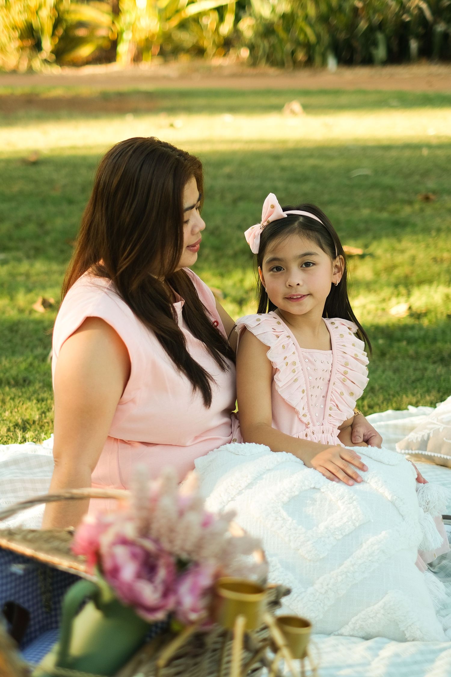 Two people enjoying a sunny picnic on a blanket with flowers in a grassy park.