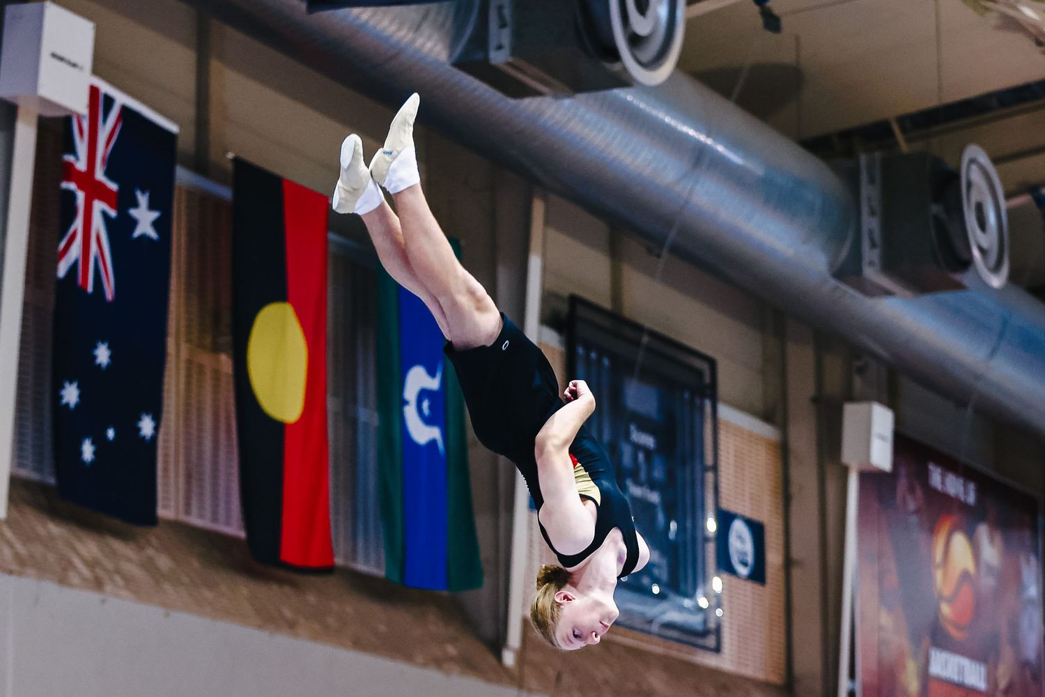 A rhythmic gymnast performs a graceful pose while holding a ball during a competition routine in an indoor arena.