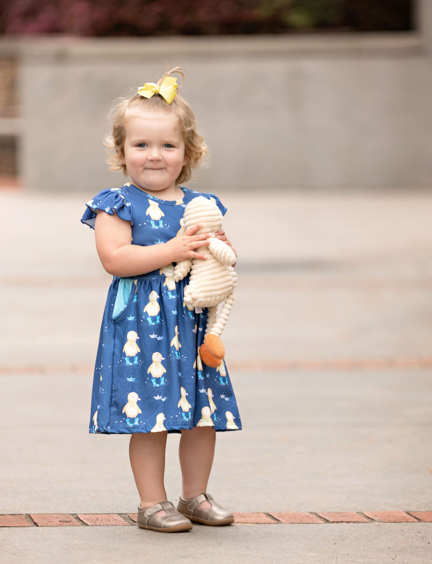 A two-year-old little girl with curls holding her duck in a duck dress. Greenville, SC newborn photographer. Easley, SC Newborn photographer