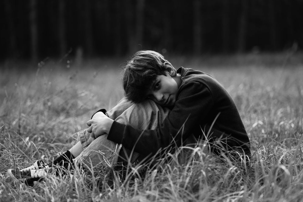 A person lies in a grassy meadow on a black and white summer day, photographed from a side angle.
