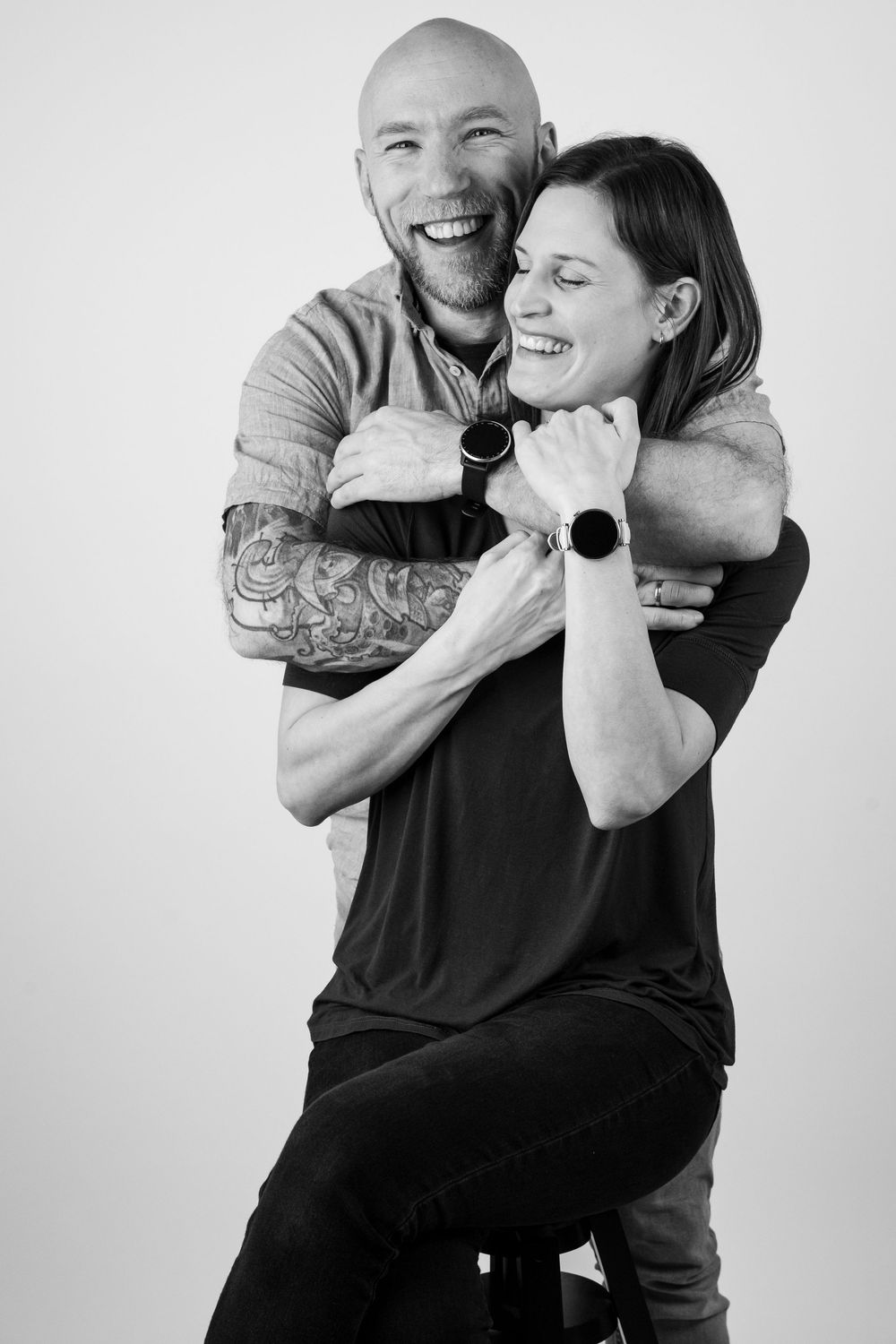 A black and white photo series showing a couple embracing and laughing together against a plain background.
