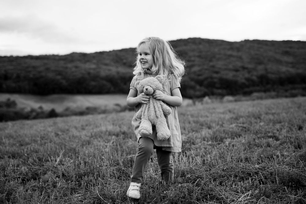 Virág stands in a grassy field against rolling hills in a black and white portrait.