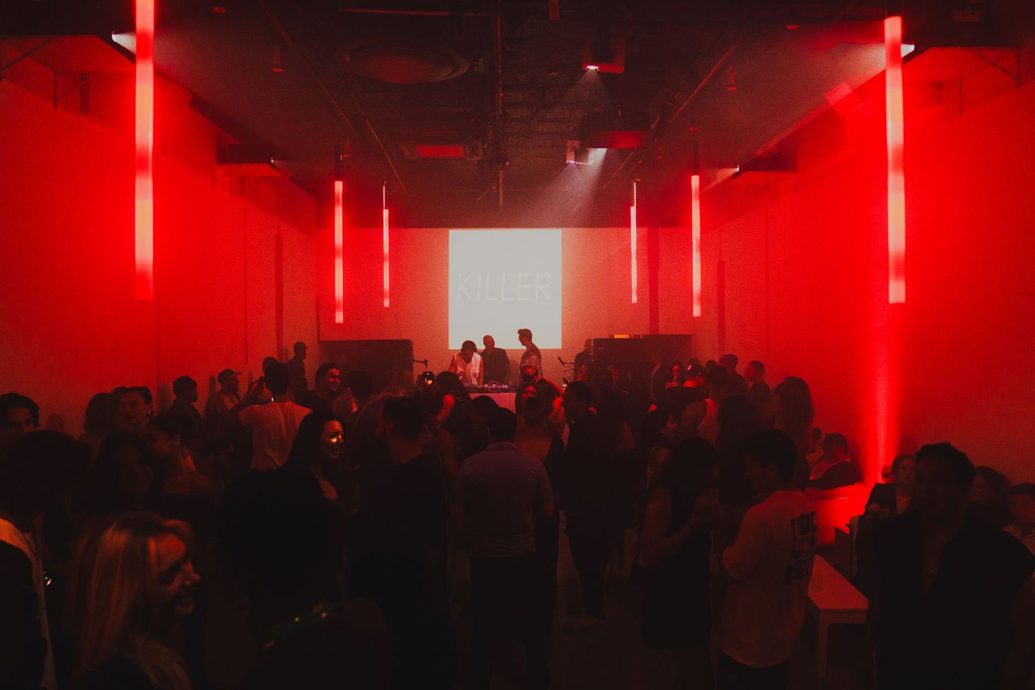 A crowded nightclub venue illuminated with dramatic red lighting and vertical LED strips.