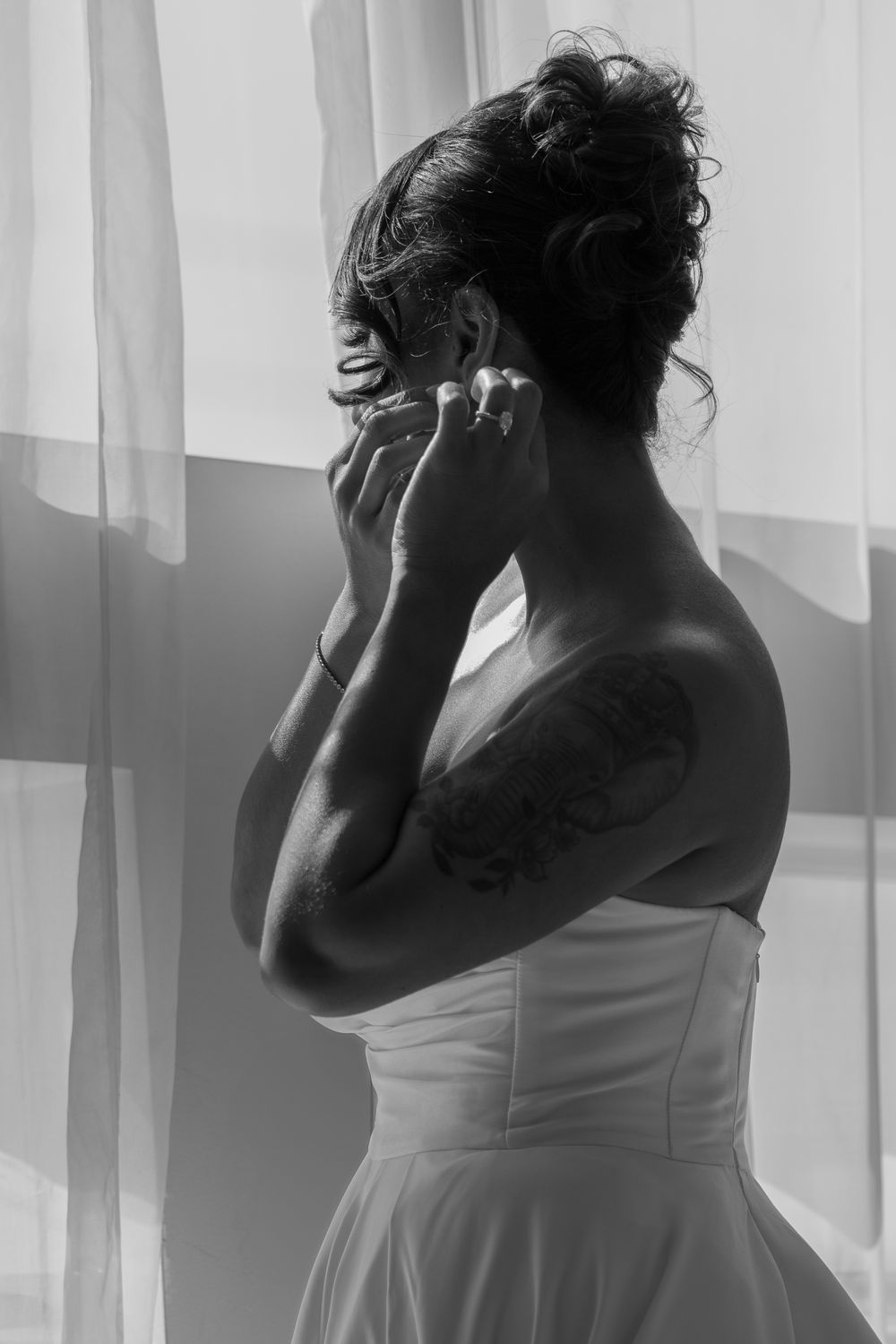 Black and white artistic portrait showing silhouette in white dress with visible tattoo by window light.