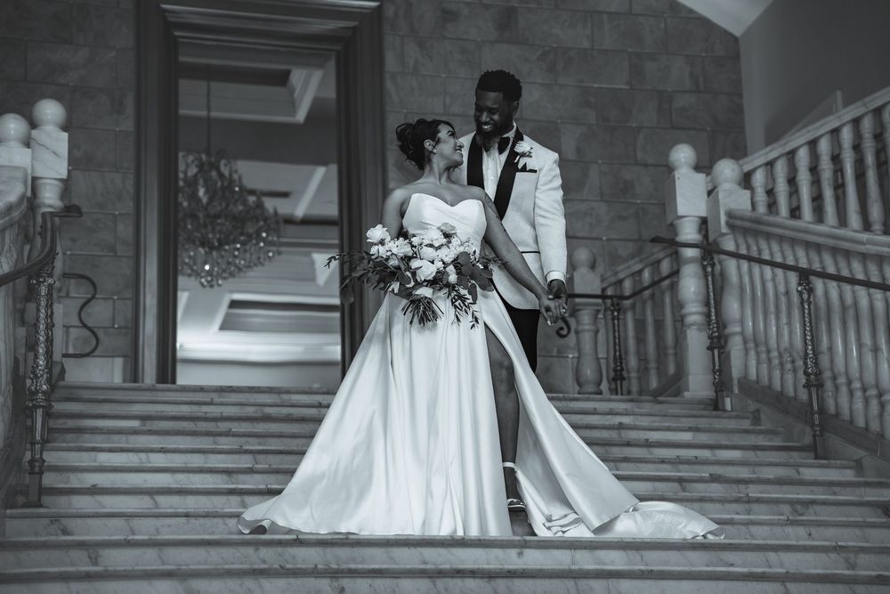 A monochrome wedding portrait showing a couple posing gracefully on stone steps, with the bride holding a floral bouquet.