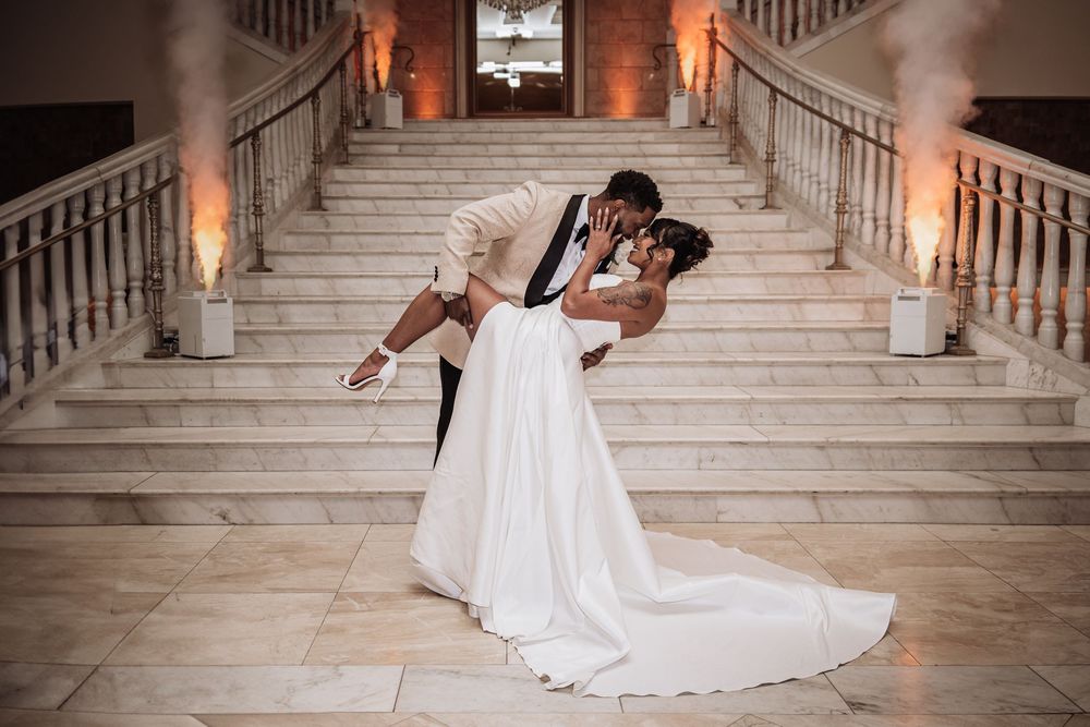 A romantic embrace on an elegant marble staircase illuminated by warm lighting during a wedding celebration.