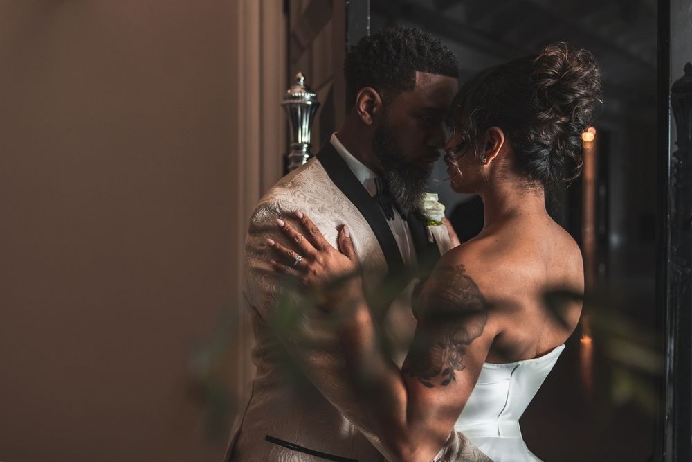 A tender moment between newlyweds embracing near a window, with soft natural light illuminating their intimate pose.