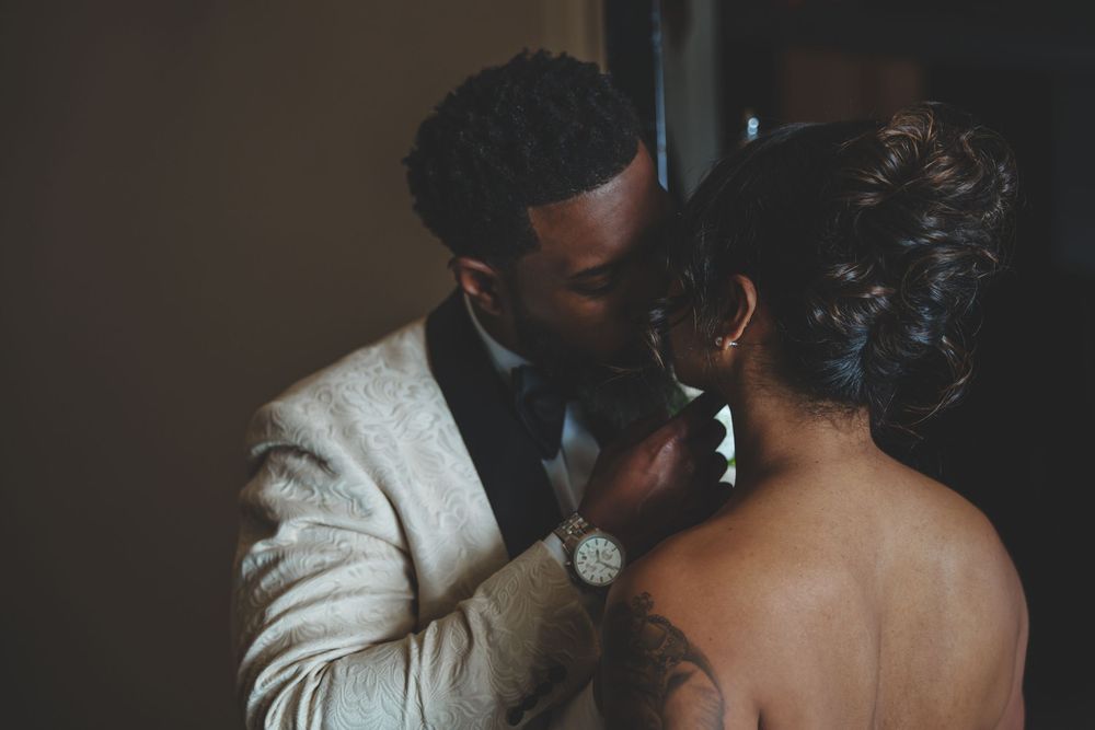 A romantic moment between a couple, with the groom wearing a white jacket and the bride in an elegant backless dress.
