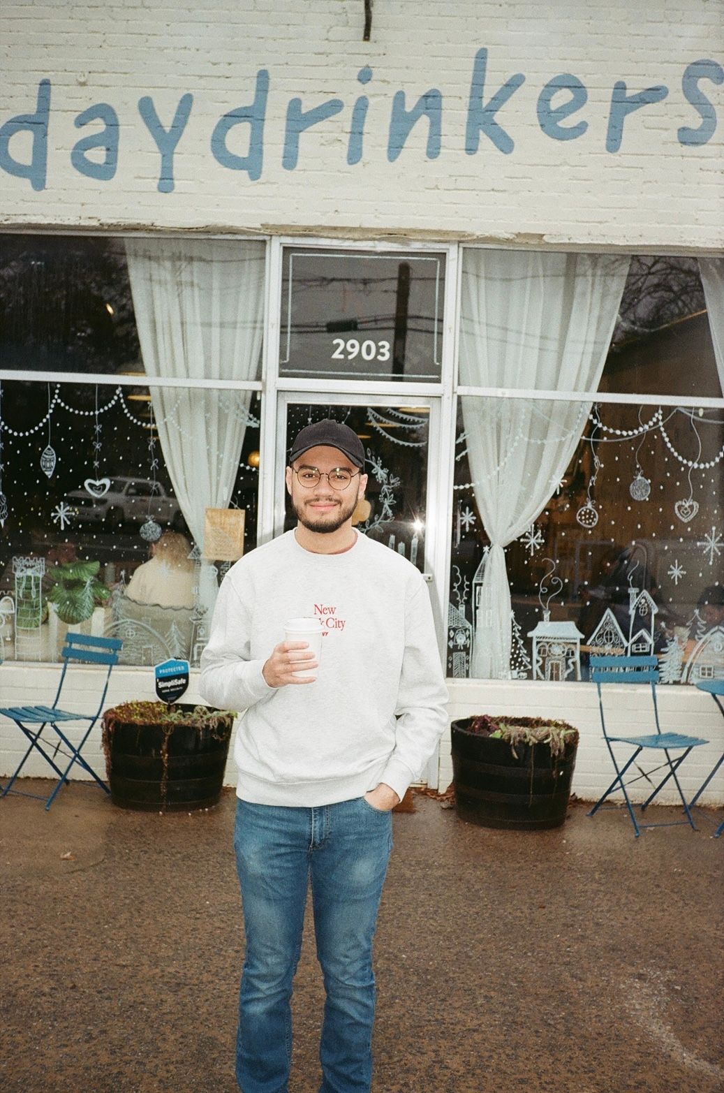 Customer stands outside Daydrinkers cafe at address 2903 with white curtains and blue chairs visible in the storefront.