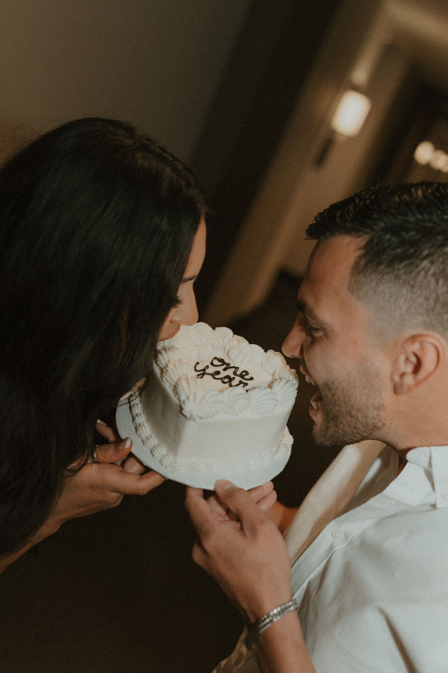 Couple sharing romantic moment while eating cake together in dim lighting.