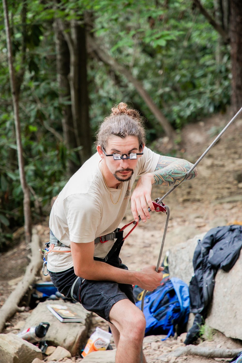 Rock climber in casual attire managing ropes at the base of a climbing route.