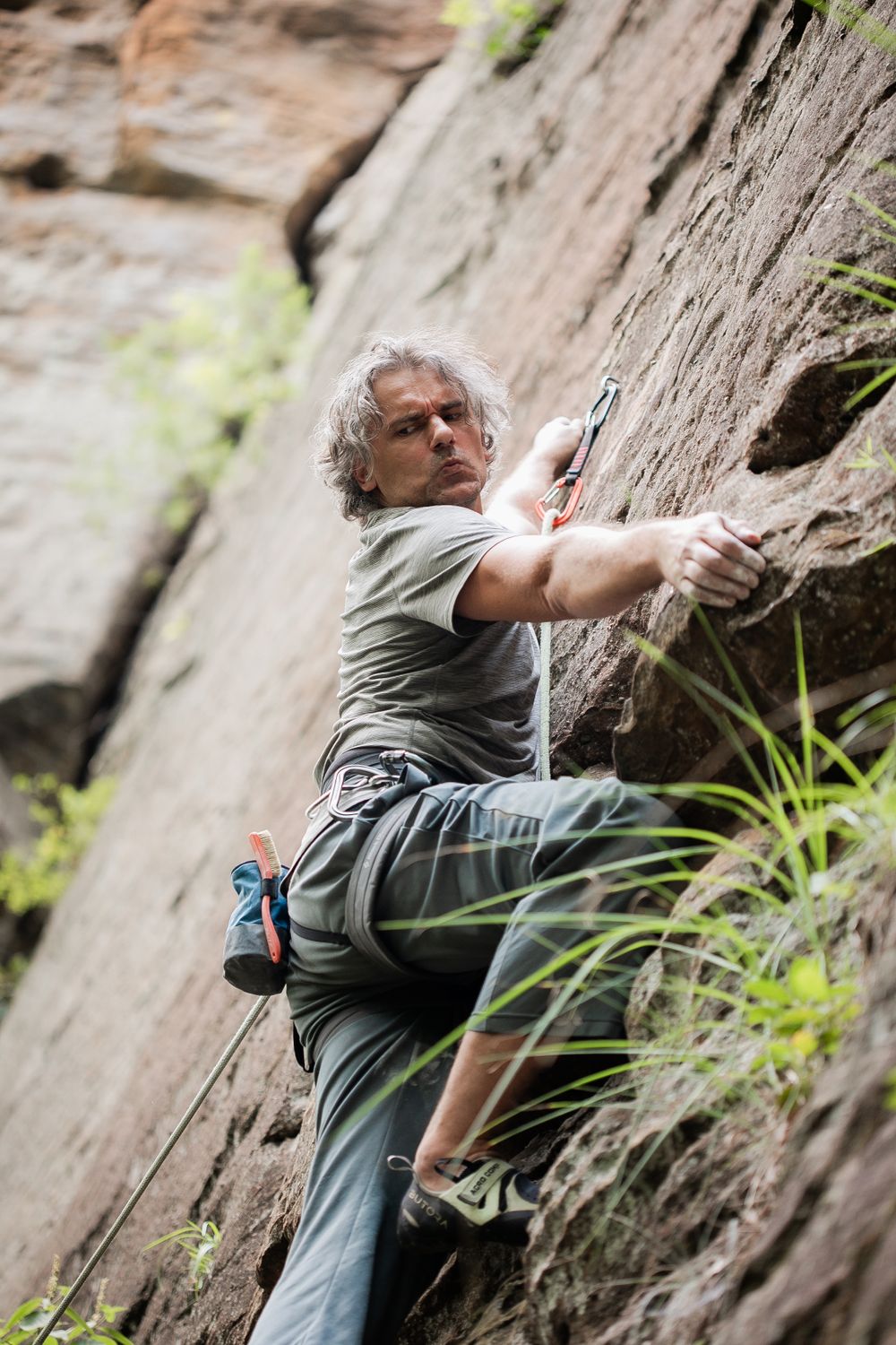 Rock climber scaling a steep cliff face while wearing safety gear and athletic clothing.