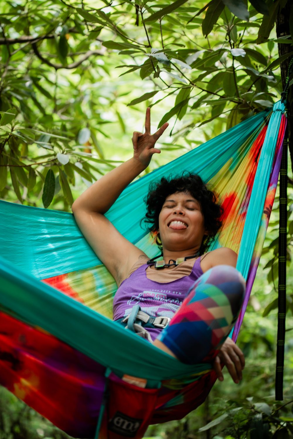 Person relaxing in a colorful hammock under green bamboo leaves making peace sign.