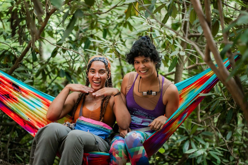 Two climbers sharing joyful moment while resting in colorful hammock surrounded by trees.