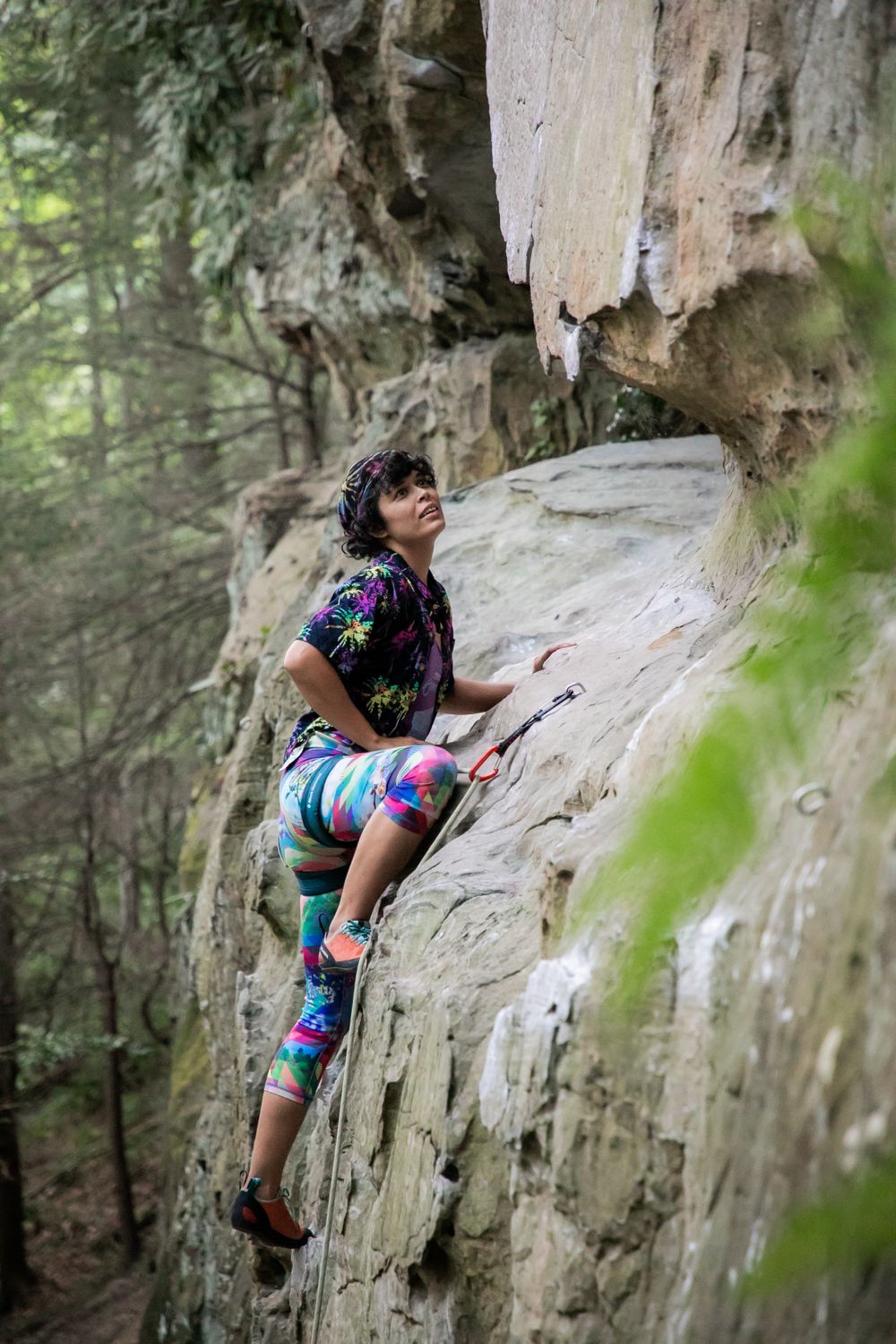 Rock climber in bright athletic wear scaling limestone cliff face in forest setting.