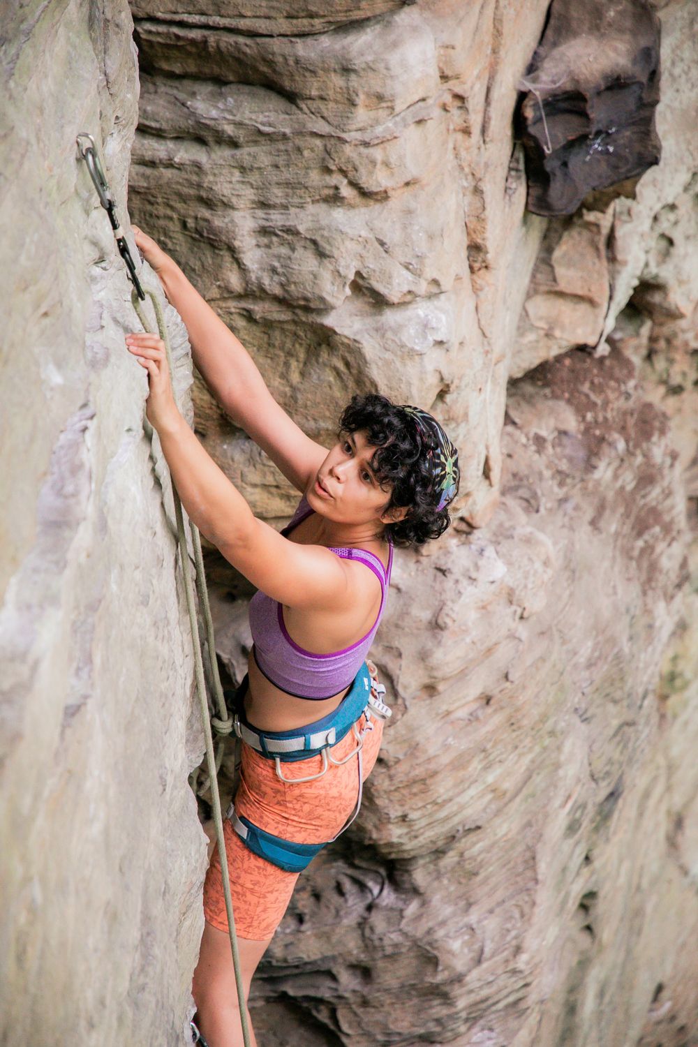 Climber in purple tank top navigating challenging rock face with precise technique.