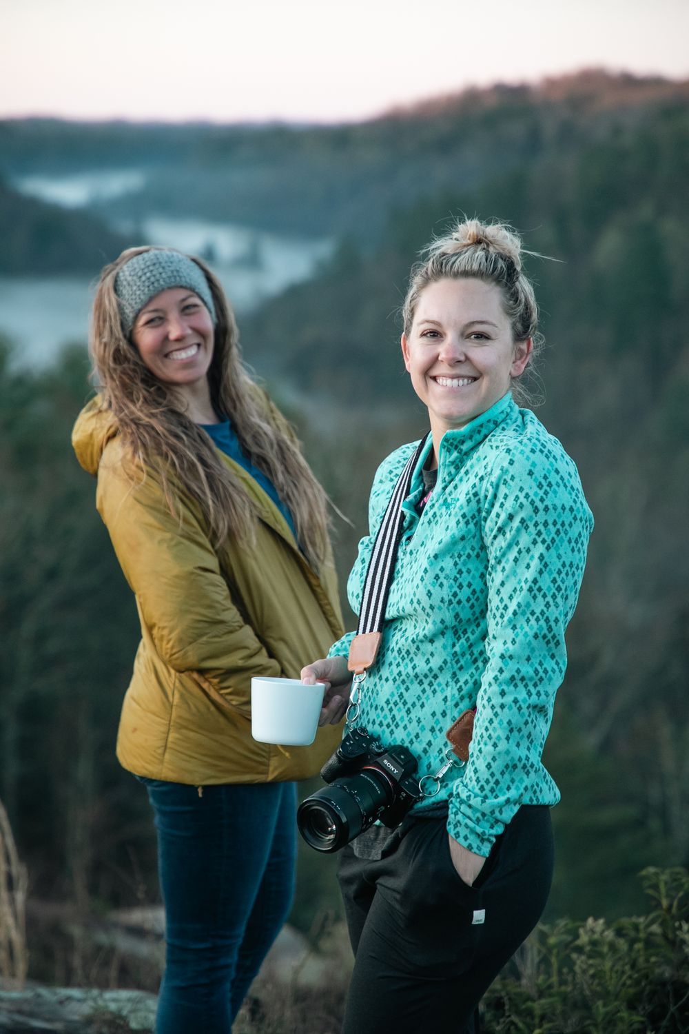 Two photographers with cameras enjoying a scenic mountain overlook at dusk.