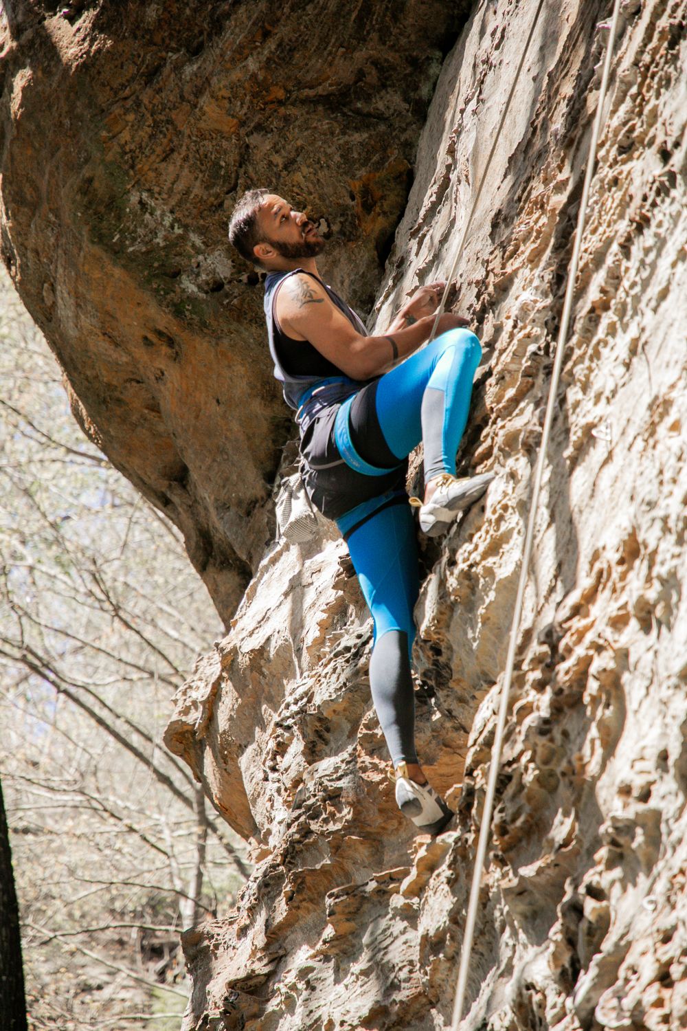 A rock climber in blue leggings scales a challenging limestone cliff face.