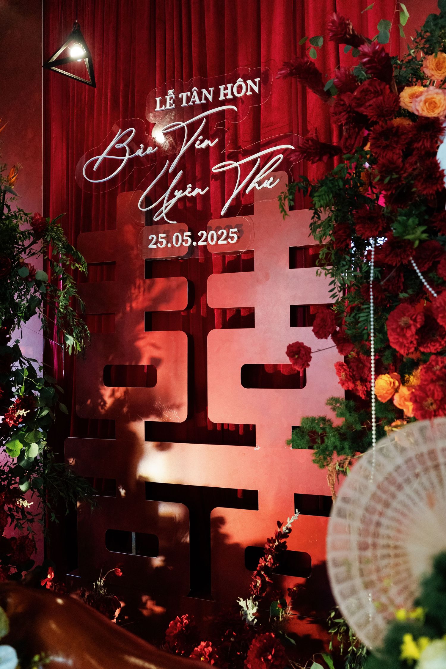 Wedding decor featuring a Chinese double happiness symbol in red lighting with floral arrangements of roses and greenery.