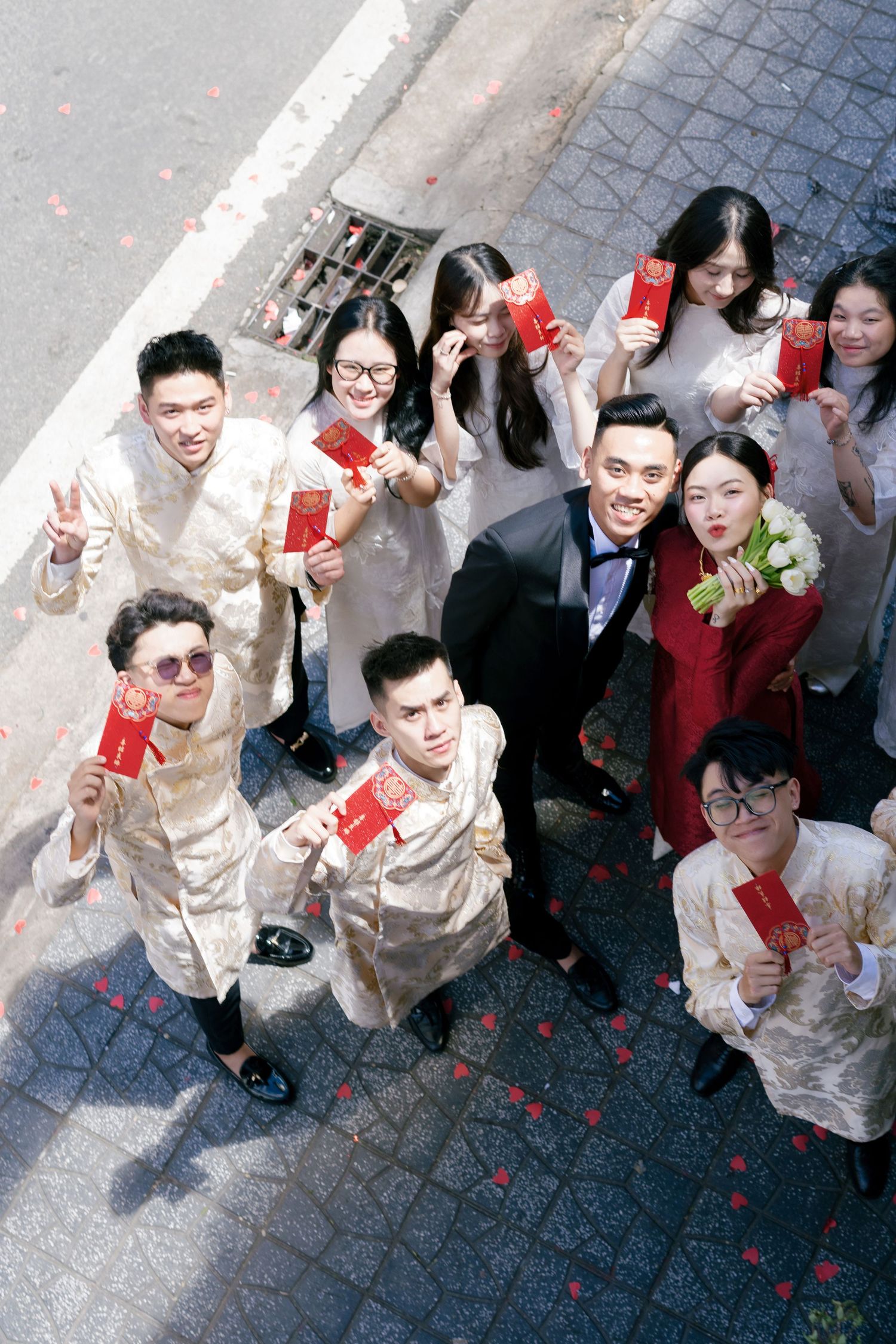 A group dressed in formal attire holds red envelopes at a traditional Chinese celebration viewed from above.