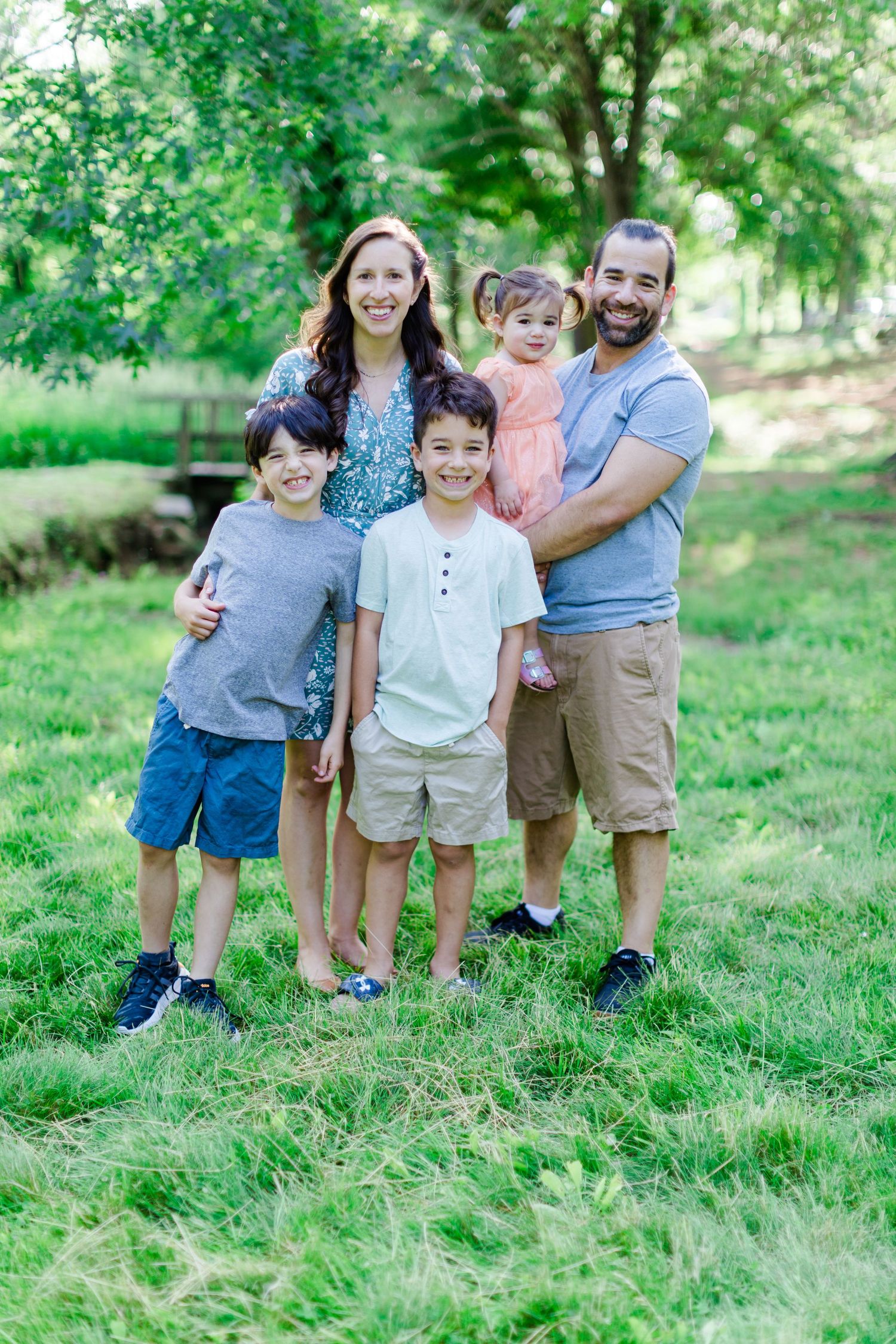 Candid family photos captured outdoors showing playful moments together on green grass in a natural park setting.