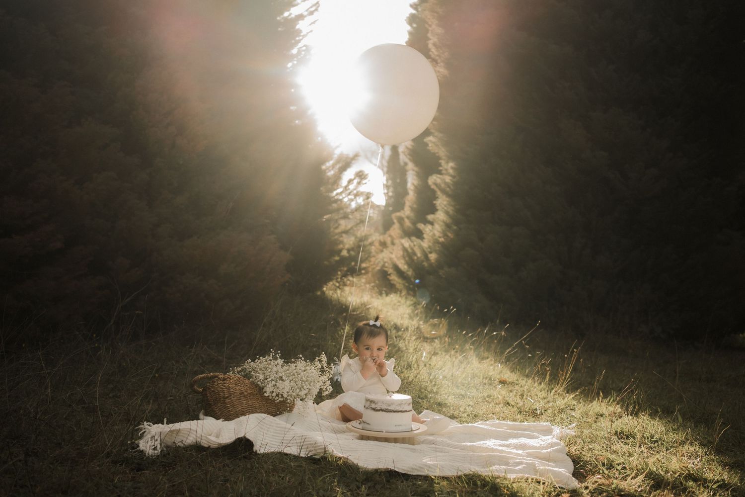A dreamy sunset photograph of someone reclining on white fabrics with books and tea in a backlit forest setting.