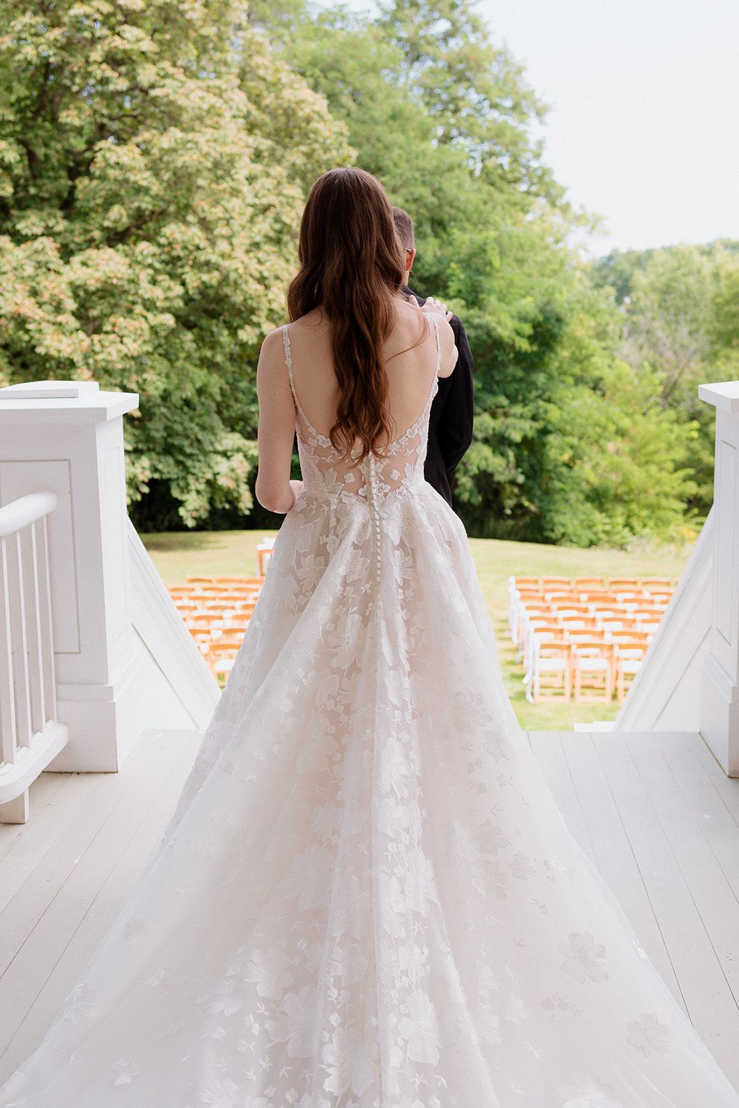 Elegant lace wedding dress with flowing train photographed from behind on a white porch with columns.