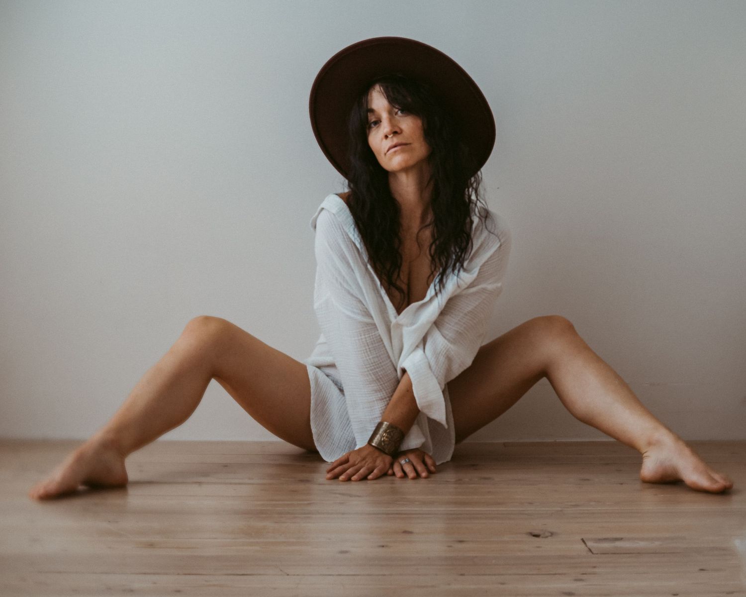 Minimalist portrait with white shirt and wide-brimmed hat on wooden floor.