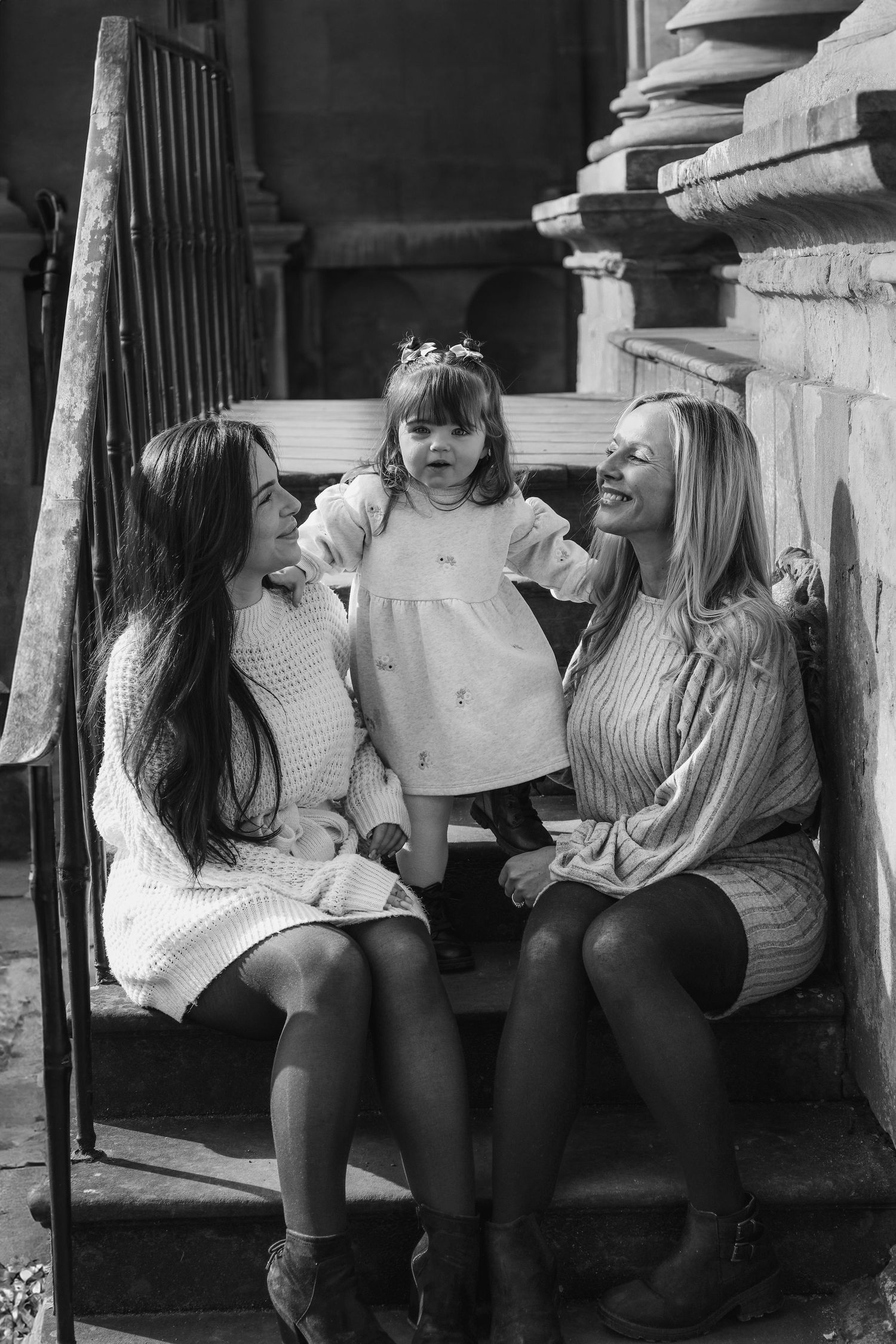 Black and white photograph of three people sitting together on stone steps during family shoot in Nottingham