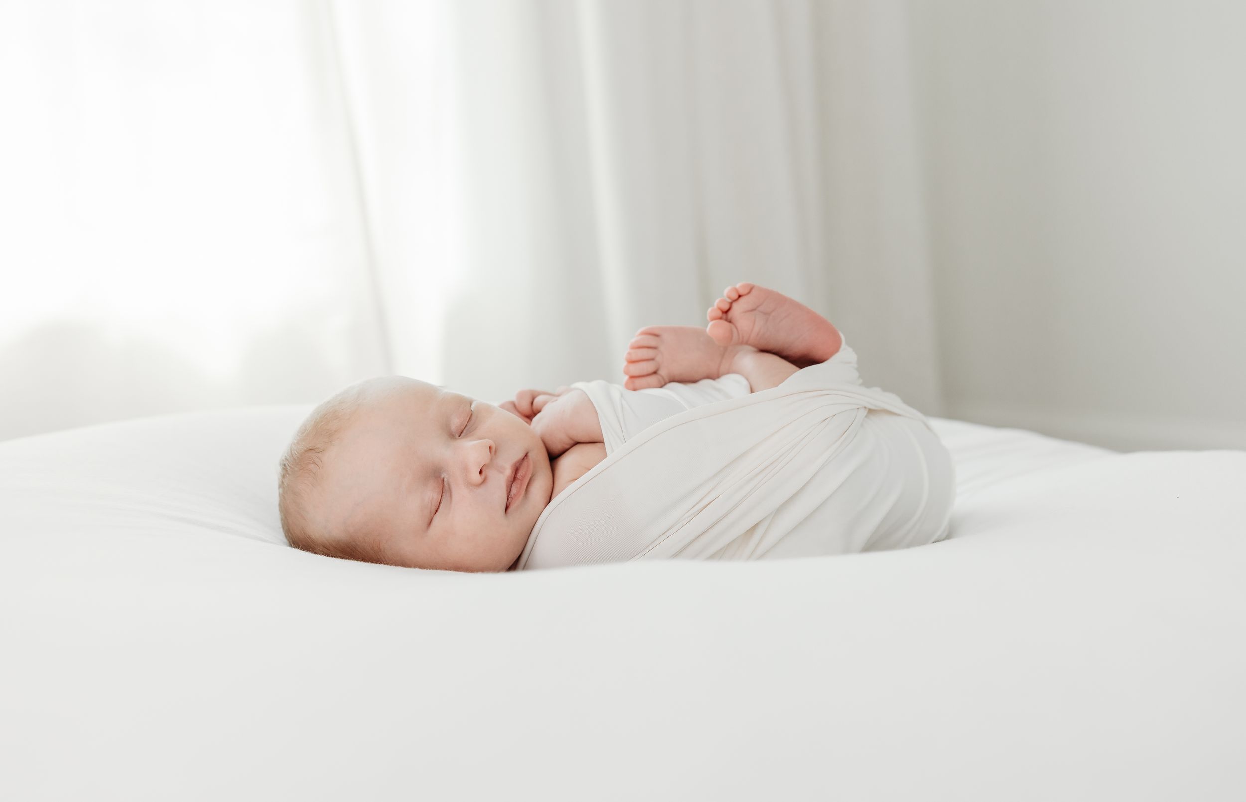Peaceful sleeping newborn swaddled in white on a soft white surface, natural light, minimalist setting.
simple timeless natural