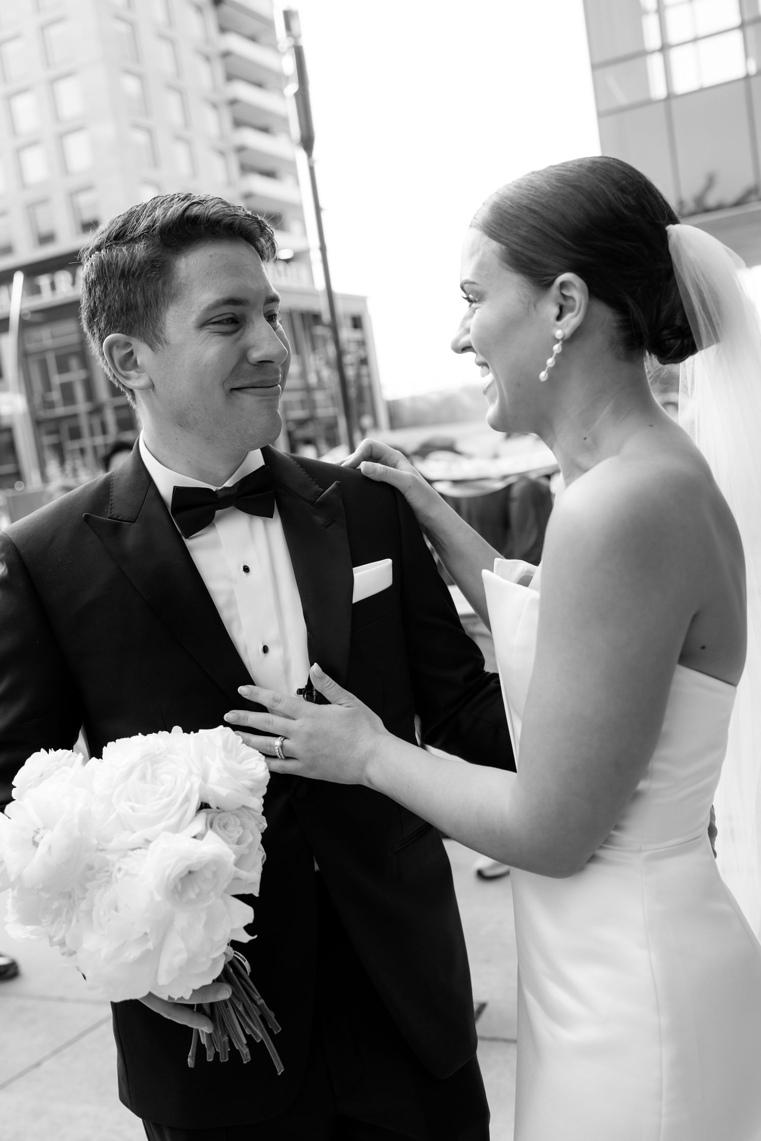 A black and white candid wedding photo showing two people sharing a joyful moment, with bride holding bouquet.