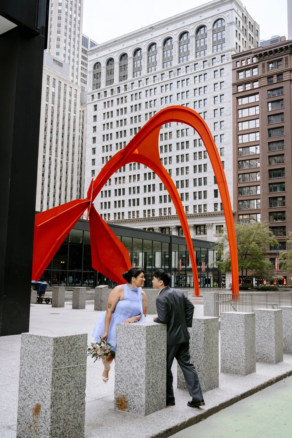 Couple standing by stone bollards near red Calder sculpture Flamingo in downtown Chicago's Federal Plaza.