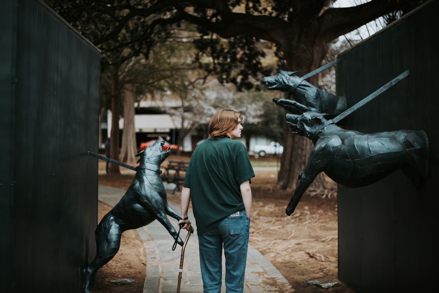 Girl with a cane walks through statues of dogs fighting off their leash.