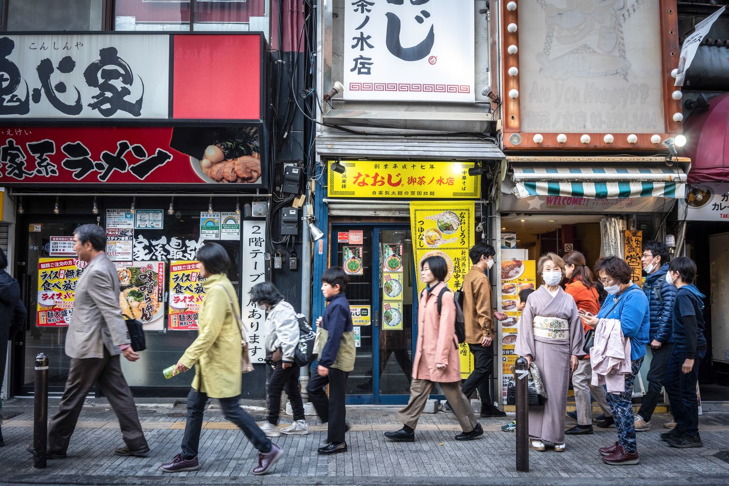 Crowded street scene in Japan with pedestrians walking past traditional shops and restaurants.