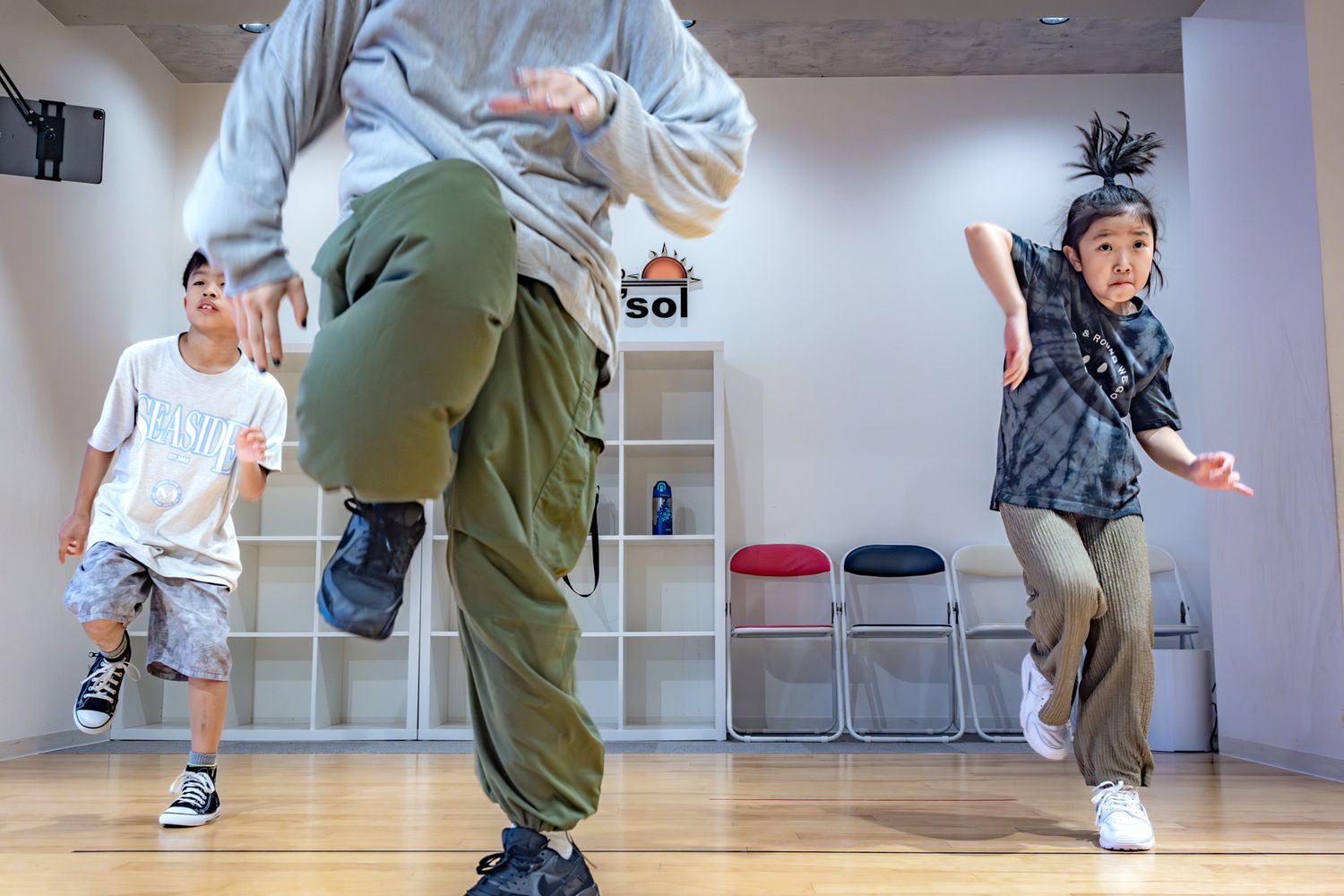 People practicing dance moves in a bright studio with white storage shelves.