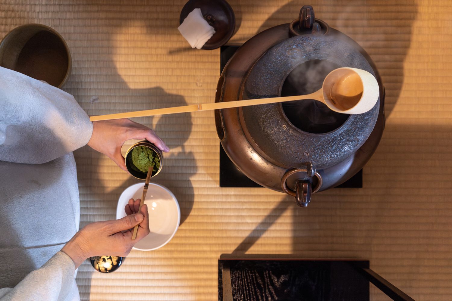 Overhead view of hands preparing traditional Japanese tea ceremony with ceramic teapot.