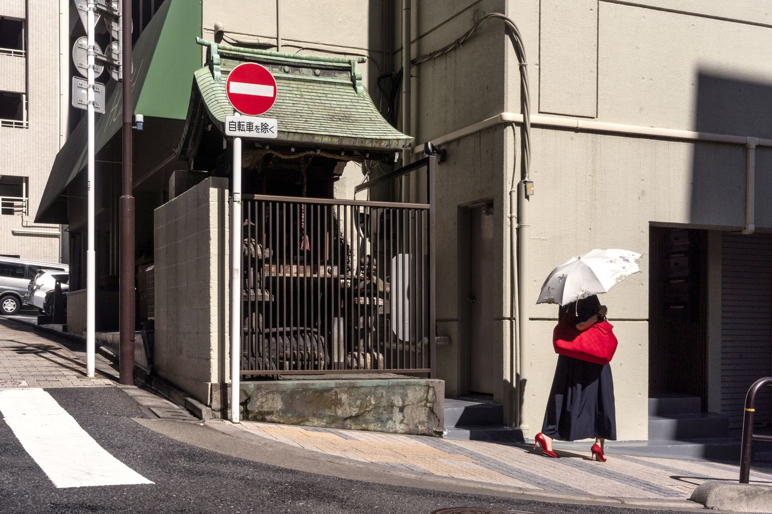 Woman in red walks past a building entrance with a no entry sign in an urban Japanese street setting.
